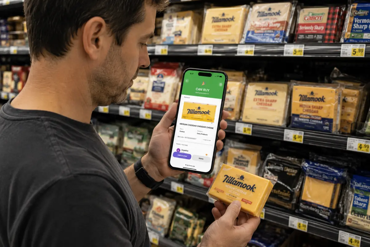Man in grocery store cheese aisle holding Tillamook block cheddar in one hand and phone with Favory app showing CAN BUY rating in the other hand — Tillamook, Cracker Barrel, Kraft, Sargento visible on shelf behind him